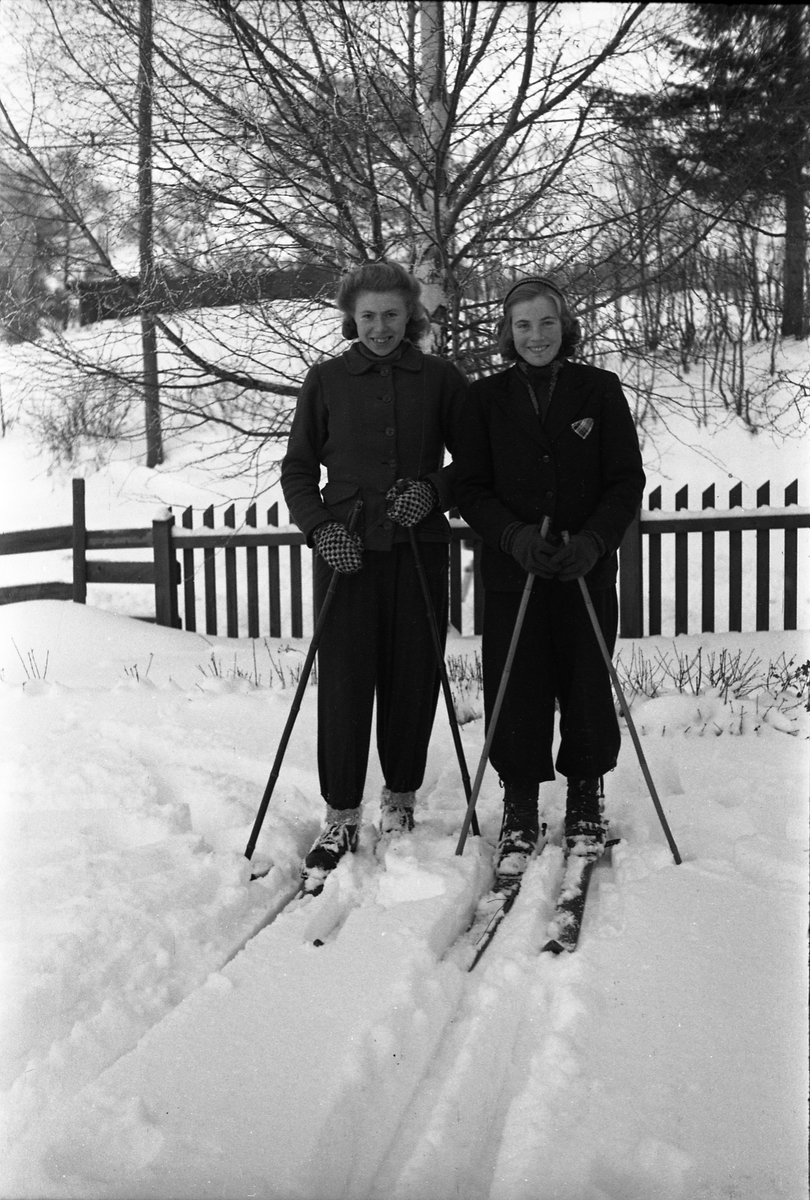 Helfigurs portrett av Olaug Rogne (til høyre på bilde 1) og Tora Johansen. Fire bilder der de to er er avbildet på ski på de tre første, sammen på det første, hver for seg på de to neste. På bilde fire igjen de to sammen, men uten ski.