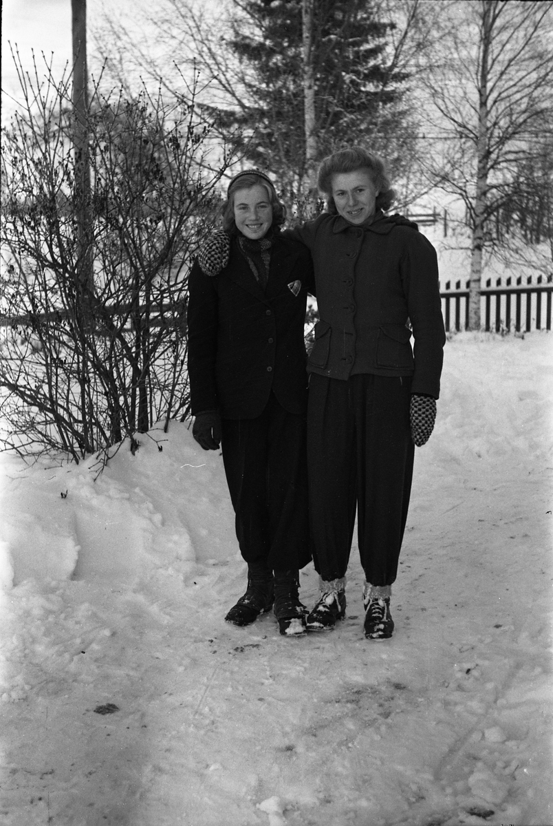 Helfigurs portrett av Olaug Rogne (til høyre på bilde 1) og Tora Johansen. Fire bilder der de to er er avbildet på ski på de tre første, sammen på det første, hver for seg på de to neste. På bilde fire igjen de to sammen, men uten ski.