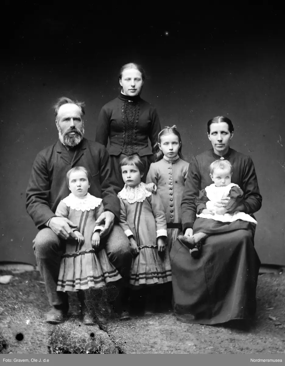 Familiebilde. Mor og far med fem barn, døtre. Fotografiet er tatt utendørs med lerret bak.