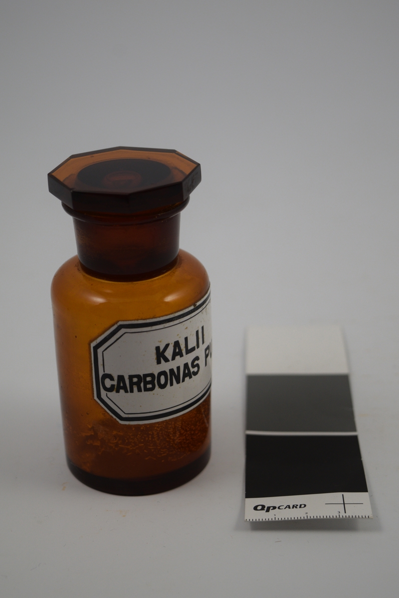 Brun glasskrukke med glasspropp. Kalii carbonas pulv. brukes til produksjon av legemidler.