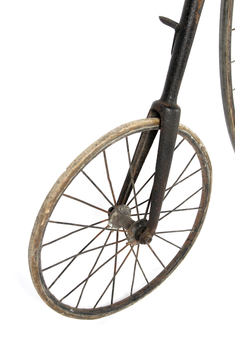 Sortlakkert velosiped med stort forhjul og lite bakhjul. Pedalene er montert direkte på fornavet og setet er plassert rett over.