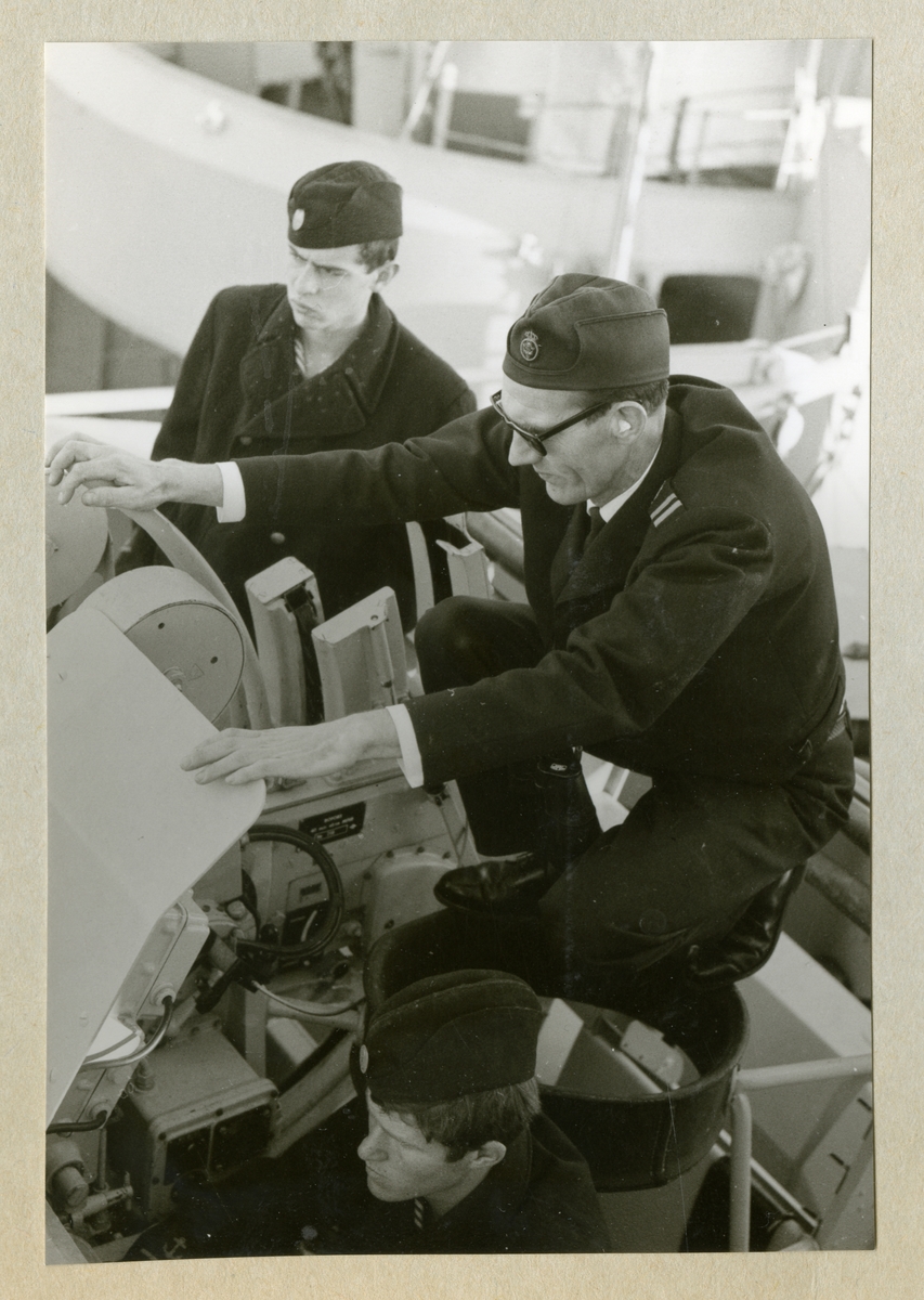 Bilden föreställer tre uniformsklädda besättningsmän vid en artilleripjäs ombord på minfartyget Älvsnabben under långresan 1966-1967.