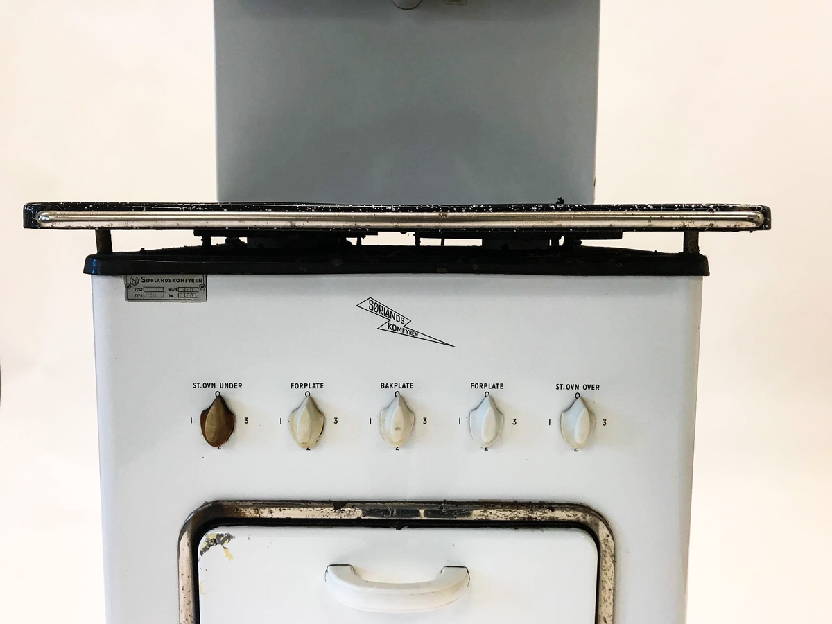 Elektrisk komfyr med bakvegg og tre kokeplater. Stekeovn med termometer på utsiden. I stekeovnen er det to tilhørende stekebrett. Lyspære på bakveggen.