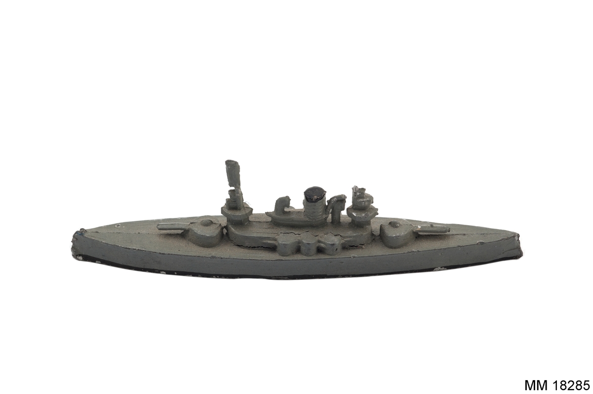 Fartygsmodell i form av pansarbåten Thor gjuten av metall i ett stycke, målad i grått, svart längs vattenlinjen. Spetsig för och akter. Plan botten. Artilleripjäser i för, akter och sidor, en skorsten, torn och mast.