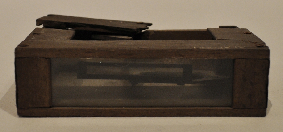 Avvägningsspegel är av Elwings modell. Rektangulär trälåda innehållande en graderad metalllinjal. Två sidor med glas. Ovandelen trasig.