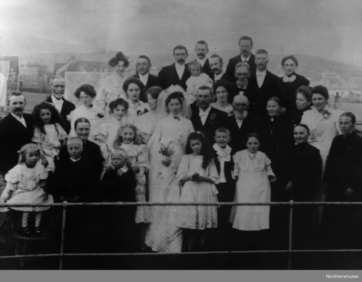 Brudepar og bryllupsgjester, stor familie, flotte kjoler. På et hustak, kanskje på et hotell? Kristiansund ca 1920. Nordmøre museums fotosamling