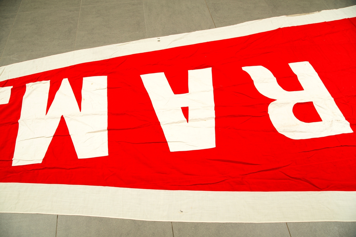 Flaggpose med vimpel. A) flaggpose i jute med tau. B) vimpel, rød med hvite bokstaver og ytterkant: FRAM. 