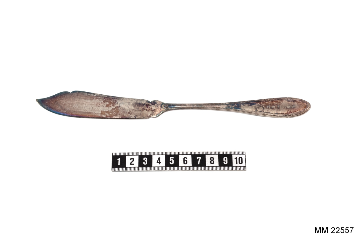 Fiskkniv, skaft med vågformad slinga längs kanten.
Märkt på skaftet: "H.M. FYLGIA" samt "KA ALPACCA 45GR".