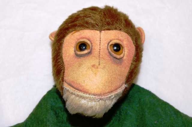 Hånddukke med fjeset til en apekatt, og grønn overdel. Apekatten har hvitt skjegg og brune øyne av glass.