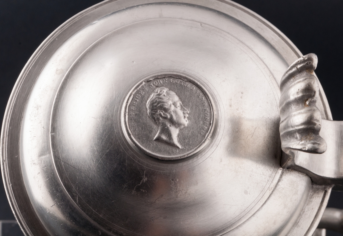 Bordkanna, tenn. På locket ett mynt med Oscar II. 
Märkt "NAS"=Nild Abraham Santesson, Stockholm 1839-1875)
"U5"=1874.