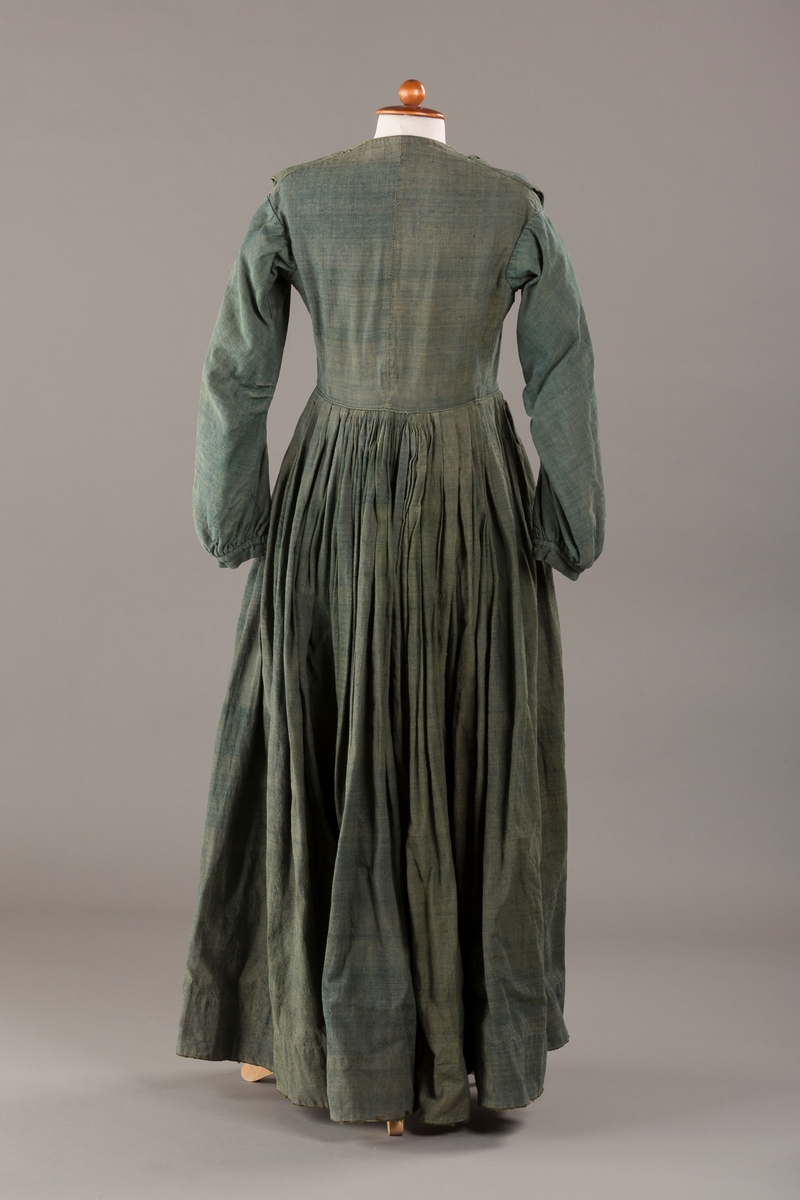 Form: Trangt liv med legg foran, skjørtet sydd med legg i livet.  God vidde i skjørtet, lange armer. Fem hekter i livet mangler.