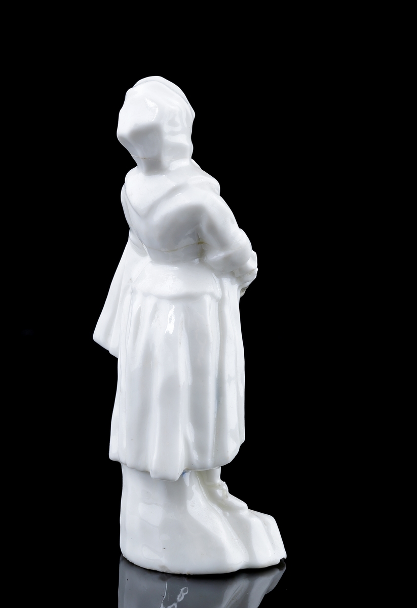 Figurin i vitt porslin, föreställande en kvinna i huvudduk och tidstypisk klädsel.
Kvinnan håller händerna överlappande framför kroppen, med en kappa hängd över ena armen, samtidigt som hon drömskt blickar snett mot himlen.