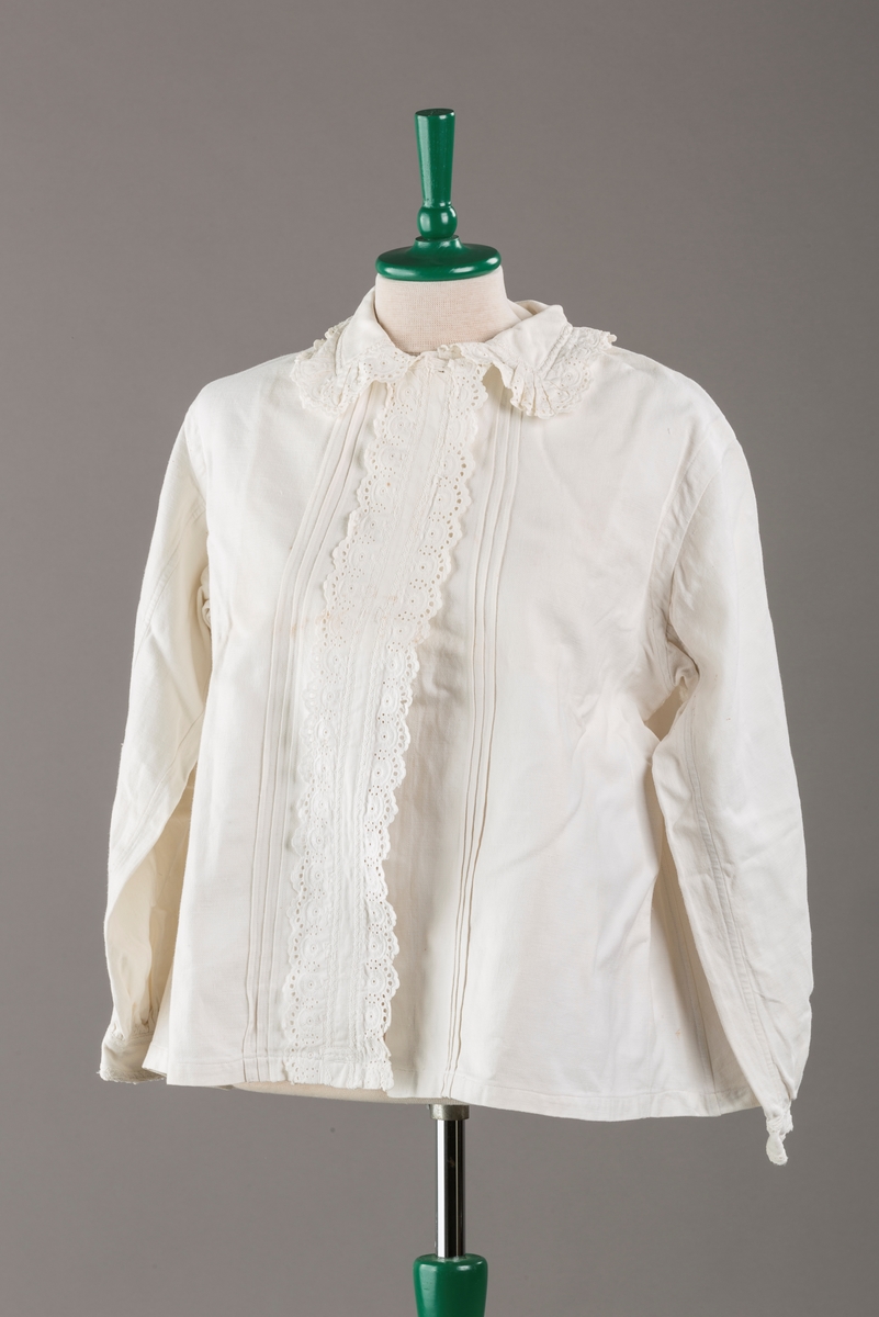 Form: Hoftelang trøye, Lange ermer, krage. Kragen og åpningen foran er kantet med  maskinprodusert blonde. Tre biser på hver side av åpn. foran. Lukkes med to løse knapper.