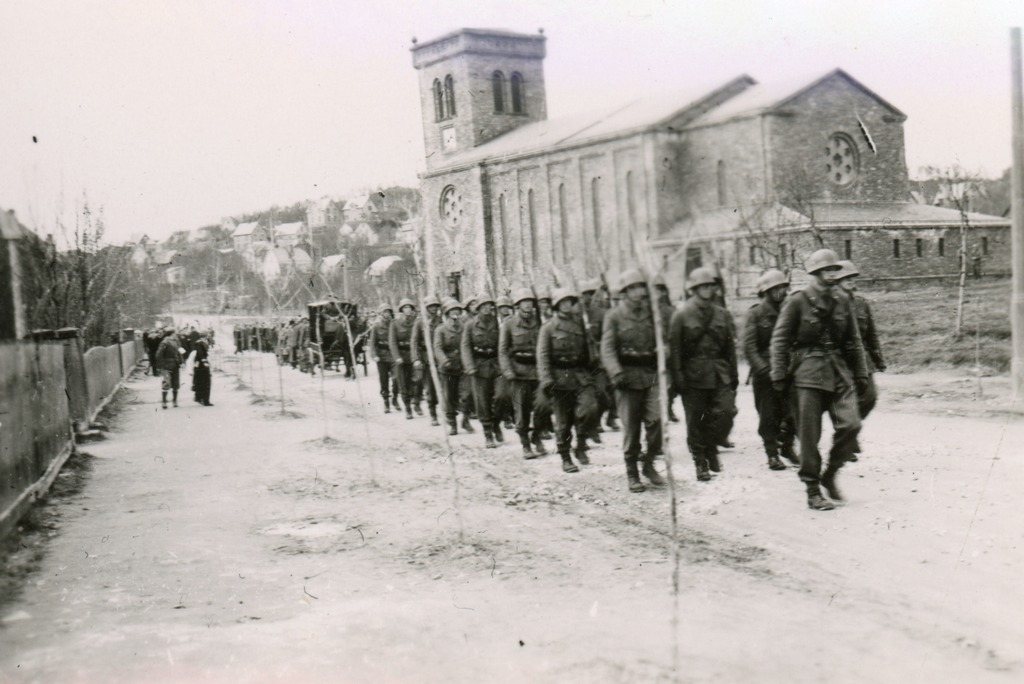 Norske soldater masjerer forbi kirken i Narvik. Det ser ut som de deltar i et begravelsesfølge.