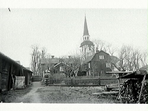 Staketomgärdad gårdsbebyggelse vid Mariefreds kyrka. I förgrunden en lada i skiftesverk och en vedtrave.