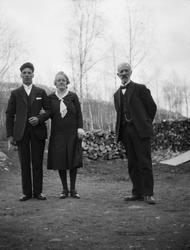 Et ungt par og en eldre mann står ute.