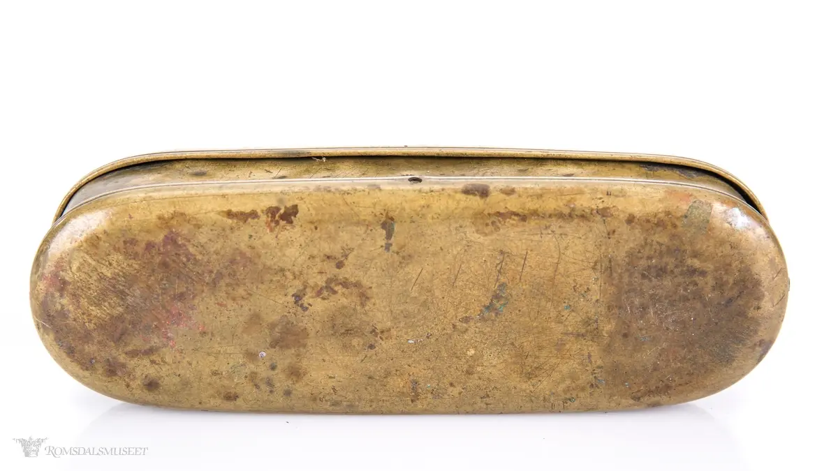 Rektangulær messingeske med avrundede ender. Har en påsatt og påklinket utenpåliggende bunn og utenpåliggende, hengslet lokk