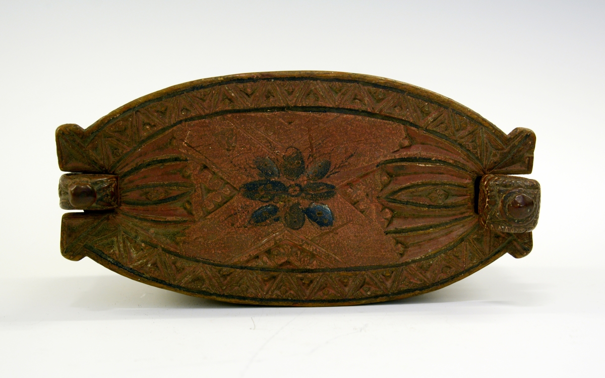 Tine av tre. Fra protokollen: Leikety-tine utskori i grovt kerbsnitt og plymrankkrullar. Under botnen skori 1814 og bokstavar. Standarane løglegt maksla som hovud med haarflettur. Raudmaala.