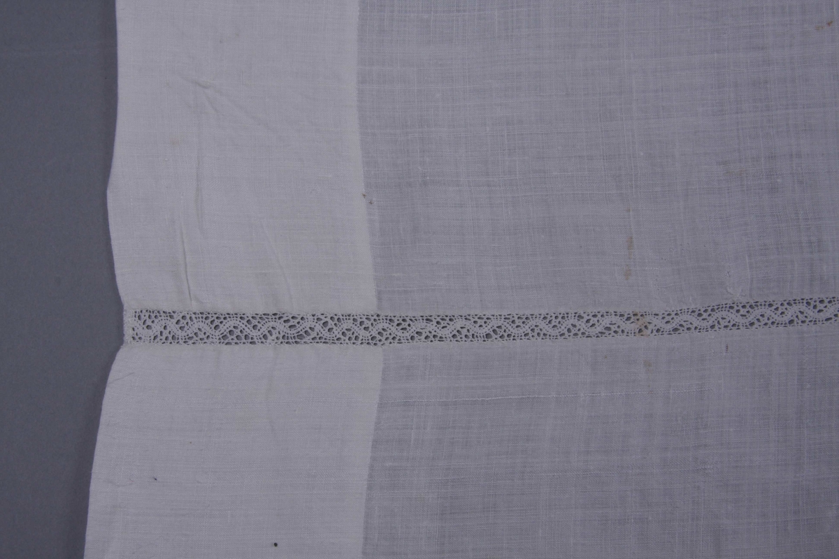 Hvit linlerret i tre bredder sydd sammen med en 1 cm. bred knipling med mønster av bølget bånd. 8 cm. bred fall på alle fire sider.