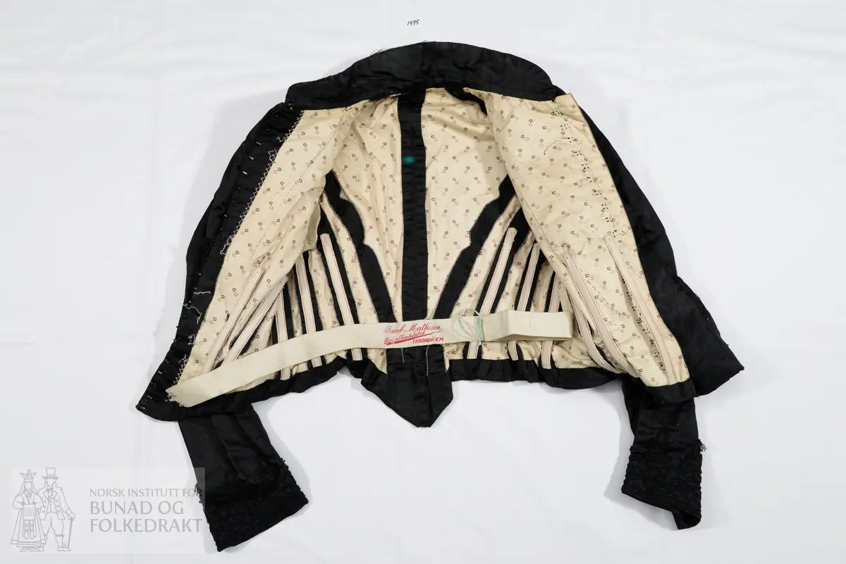 Kjoleliv til skjørt NBF2017-1494 i svart silkesateng med skrålagte folder og kjøpeblonder i svart.  Foret med trykt bomullsfor. Tilbaketrukne sidesømmer og søm midt bak. Tosømsermer. Tre og to spiler på hver side midt framme. Tre spiler på hver side av ryggen (i sidene). Høy krage i halsen, som er avrundet ned mot midt framme. Lukking midt framme med en tett rekke hekter, 24 stk. Tre legg og en bred blondekant på skrå over brystet. Skrå lukning med overlivet på venstre side. Fire hekter har trolig vært festet på i tråhemper på høyre side av livet, på skrå. Noen rester er så vidt synlige. Livet er trolig ikke omsydd. Livet har i siste del av bruken vært brukt nedi skjørtet, tydelig på grunn av bøy i spilene og de to øyehektene midt bak på livet hvor stakken/køen har hengt. Rynket ermetopp. 
Ermene har påsydd blonde som mansjett, og har splitt med hekter til knepping.