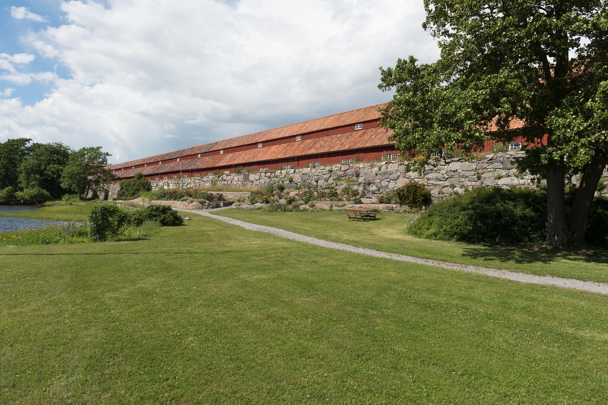 Fotodokumentation av byggnader på Lindholmen i Karlskrona. Reslagarbanans södra sida. Repslagarbanan är en av Karlskronas äldsta bevarade byggnader. Träbyggnaden är över 300 meter lång (1000 fot). Byggnaden tillkom på 1690-talet. Här tillverkades fram till år 1960 alla typer av tågvirke för seglande örlogsfartyg. I banhuvudena förbereddes hampan, råvaran till repen. När repslagarna slog repen gick de omväxlande framlänges och baklänges genom banan. År 1969 blev Repslagarbanan byggnadsminnesmärkt.