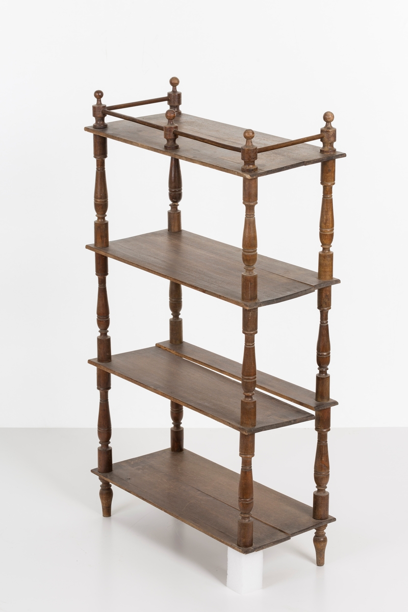 Hylle med 4 hyller. Dreide stolper mellom hyllene. Mangler ett bein. Sprosser øverst. Lakkert i mørk brunt.