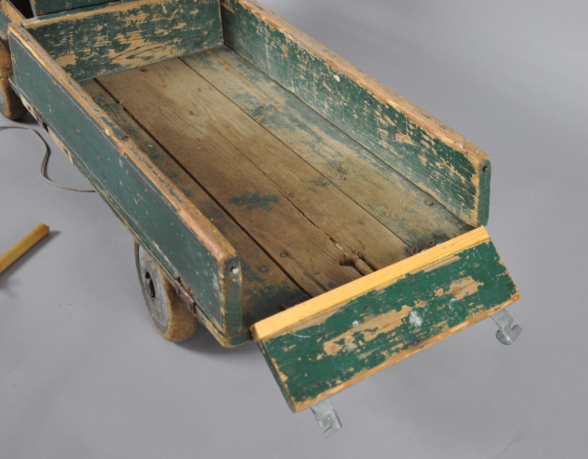 Håndlaget lastebil av tre. Består av frampart og lasteplan, samt bevegelige hjul. Lastebilen har en grønn grunnfarge med røde dekorstriper. Malingen er avslitt flere steder. Lasteplan og panser er hengslet slik at det kan tippes. Bak- og sidedør på lasteplanet er også hengslet slik at de kan legges ut. På framsiden står det en pinne ut på høyre side, på venstre side skal det være en tilsvarende pinne, men denne har knekt. På framsiden er det festet en tråd med pinne i enden, for å dra lastebilen.