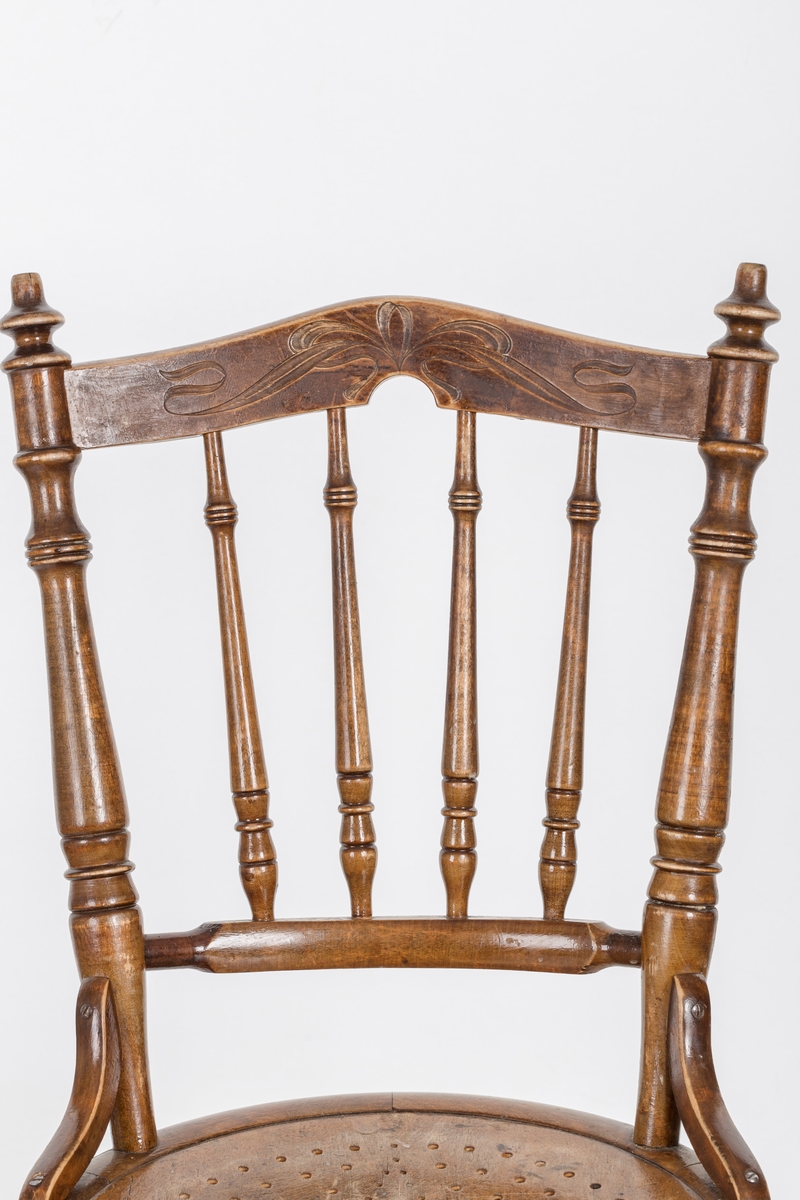 Stol i lakket treverk. Rundt stolsete med hullemønster. Rygg som er svakt buet med spiler og mønster. Dreide ben og spiler i rygg.