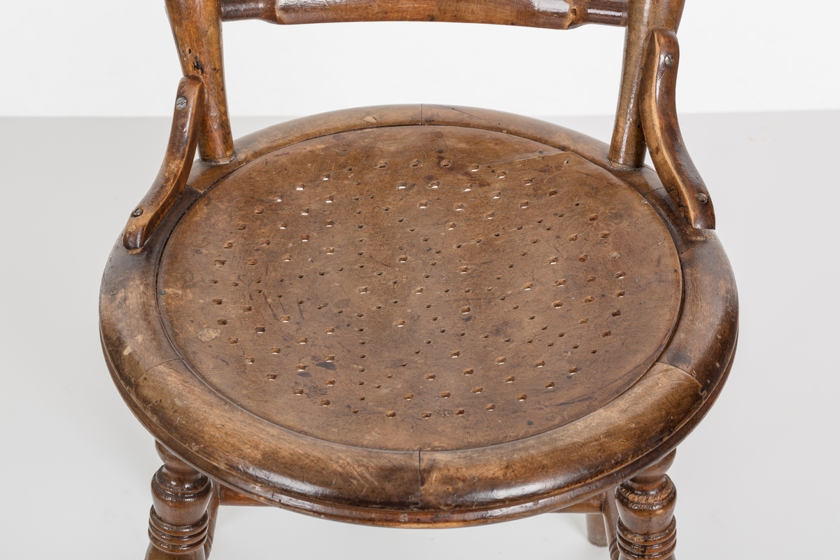 Stol i lakket treverk. Rundt stolsete med hullemønster. Rygg som er svakt buet med spiler og mønster. Dreide ben og spiler i rygg.