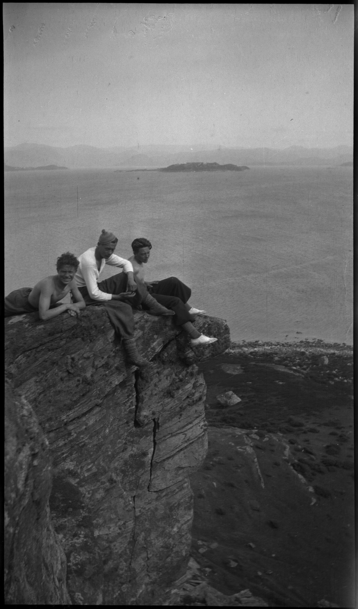 Harald Bergsaker, Ottar Roaldsøy, L. Fosse og Lindtner på den søndre enden av øya Hidle, øst for Stavanger. De er på kanten av et stup og hviler i gresset under stupet. En av dem ser utover sjøen med kikkert. Seilbåten "Vilja ligger i bakgrunnen.