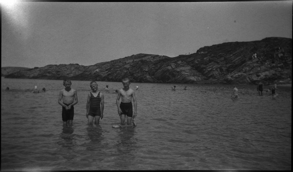 Barn og unge på og rundt stranda i Vigdelsvika. De fleste har satt opp telt, noen soler seg og noen bader. Den ene gutten på bilde nr. 6 holder et flytebelte.