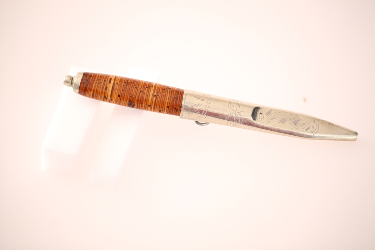 Kniv og slire hører ikke sammen. skaftet er laget av never, og slira er laget av nysølv. vanligvis hadde neverskaftkniver lærslire, og nysølvslirer hadde vanligvis ibenholdtskaft. Dekoren på slira er gravering og motivet er såkalte "Elstadkvister" slira er dermed høyest sannsynelig laget i Kolbu av en av Elstadkarene. Kniven har et fabrikkblad og er av ukjent opprinnelse.