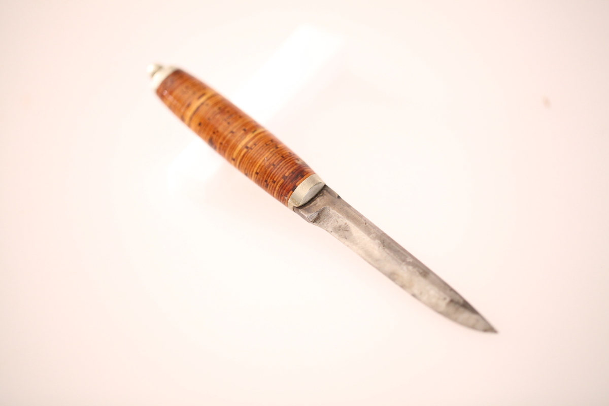 Kniv og slire hører ikke sammen. skaftet er laget av never, og slira er laget av nysølv. vanligvis hadde neverskaftkniver lærslire, og nysølvslirer hadde vanligvis ibenholdtskaft. Dekoren på slira er gravering og motivet er såkalte "Elstadkvister" slira er dermed høyest sannsynelig laget i Kolbu av en av Elstadkarene. Kniven har et fabrikkblad og er av ukjent opprinnelse.