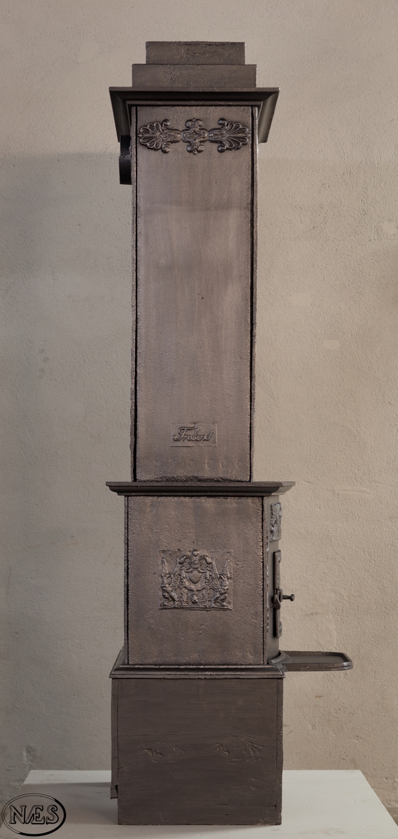 Ovnen består av to avdelinger. Underdelen har et frembuet midtparti med kamskjell flankert av sjødyr på hver side. På kortsidene skjold, løvehode og symmetriske ørner. På bakplate en krukke med symmetriske engler.
Overdelen er høy, firkantet med tredelt åpning. Empire ornamentikk og avtrappet topp. Øverst på frontplaten symetriske fabeldyr (pegasus) vendt mot hverandre.