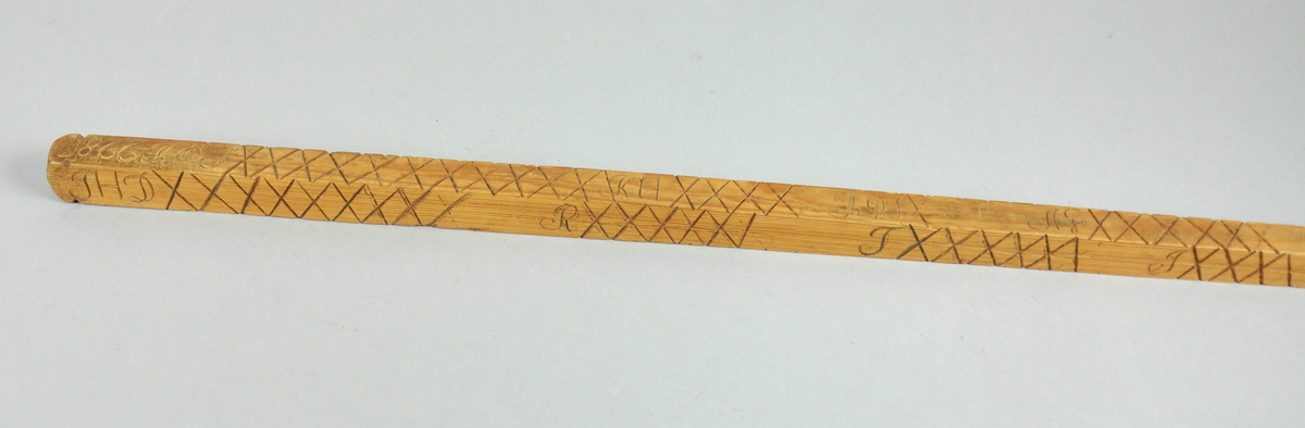 Målestokk av tre som er spiss i den ene enden. Det er inngravert mange kryss og punkter alle på fire langsider med signaturer for hver rekke av merker.