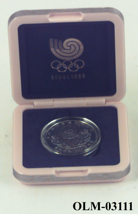 Mynt som viser to barn p den ene siden og og seks lotusblomster under jing yng symbol på den andre siden. Mynten ligger i en sølvfarget eske merket Seoul 1988.