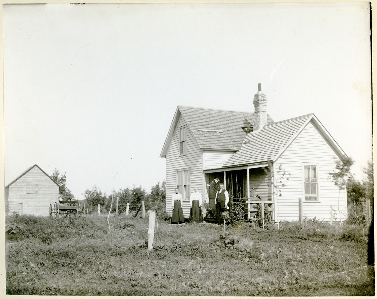 To kvinner og en mann står utenfor våningshuset på en farm i Amerika.