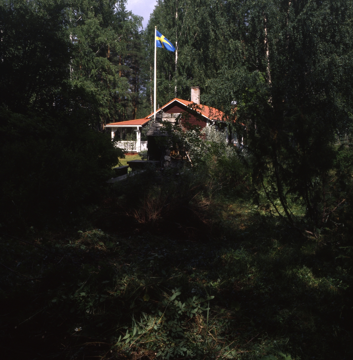 Författaren Albert Vikstens torp vid Ängratörn 1999. Huset och den murade utegrillen ligger inbäddat i grönska och flaggan är hissad.