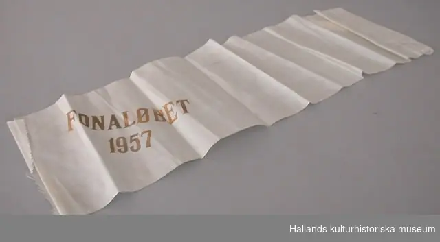 Vitt konstsidenband med målad guldtext: "FONALÖBET 1957".