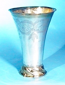 Cylindrisk bägare av silver på godronnerad fot, utsvängd mot brädden. Bägaren är förgylld invändigt och på foten samt har stiliserad blomdekoration.