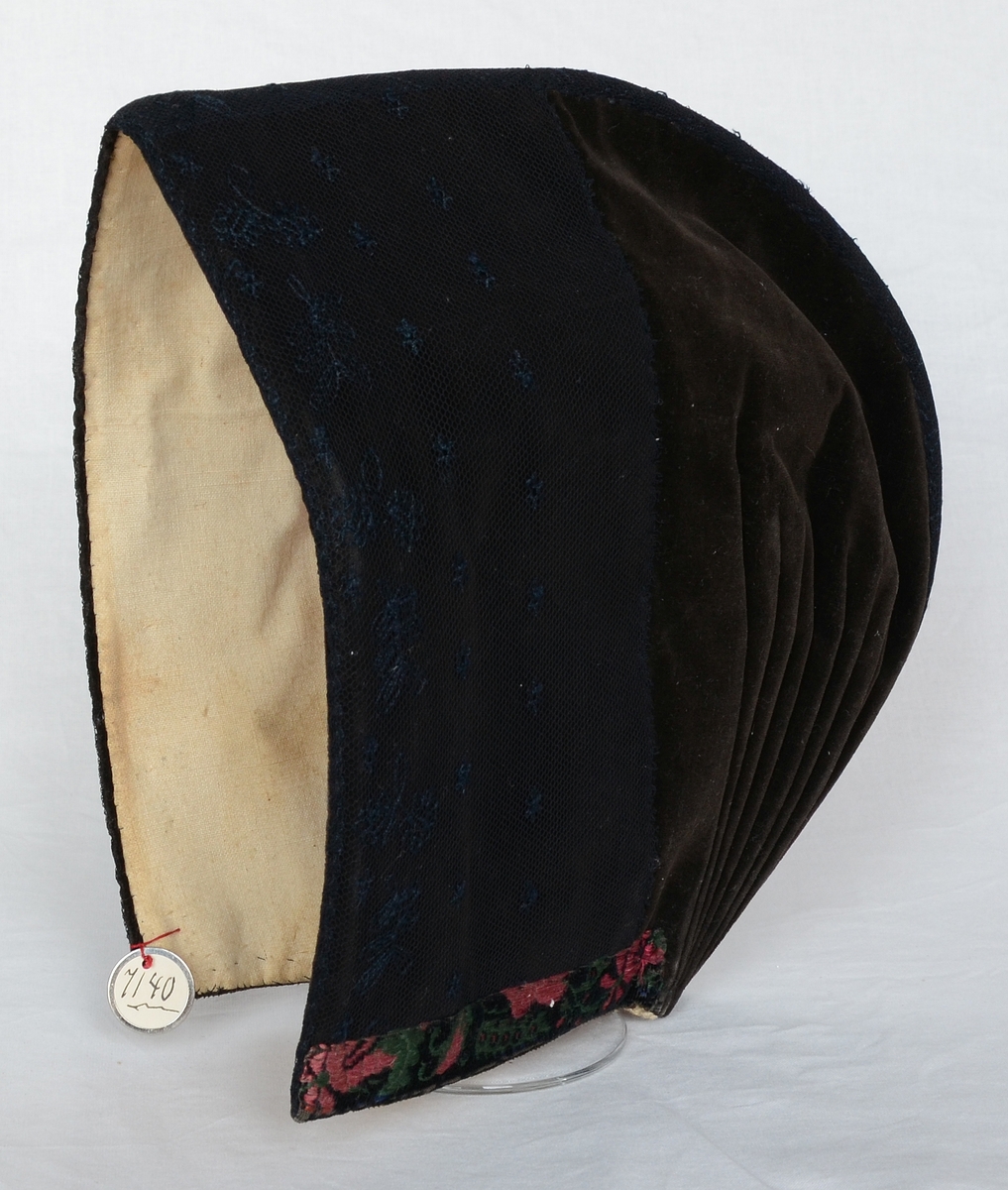 Mössa för kvinna, av brun sammet med kantband i grönt och rosa. Kallades "skreftamössa" och användes vid nattvardsgång.