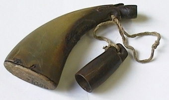 Kruthorn av horn med bottenplatta av trä, fäst med järnstift. Stängningsplugg saknas. Ett krutmått sitter fäst i hornet med ett snöre.