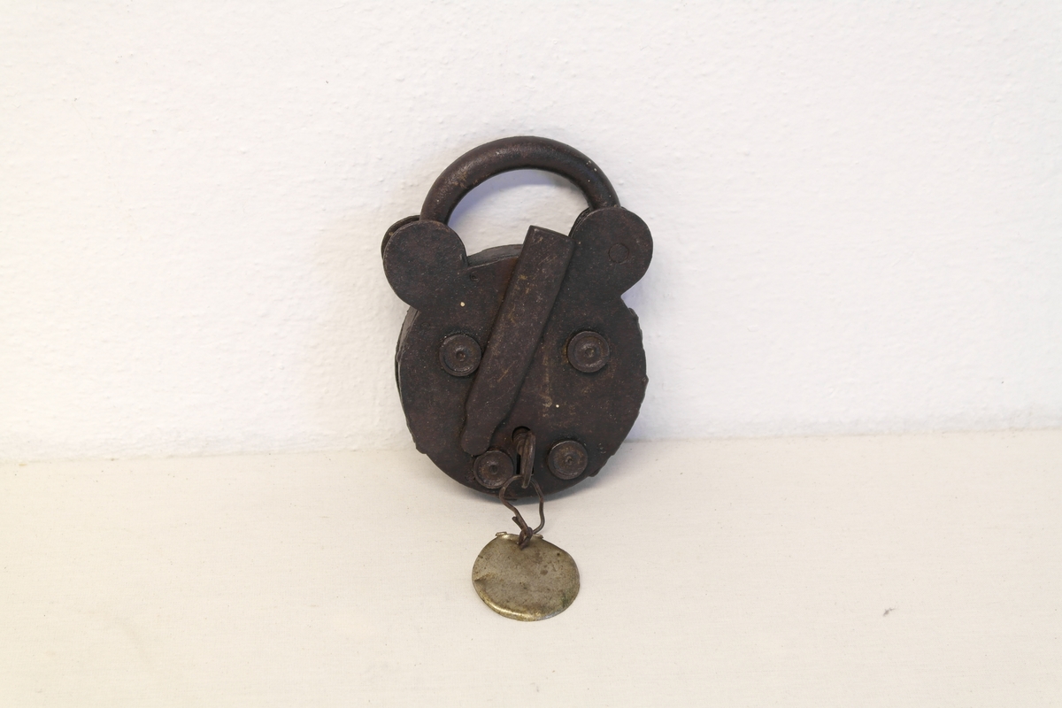 Hengelås (A) i jern. Sirkelform med bøyle. Nøkkelen står i. En rund messingplate (B) er festet til nøkkelen.