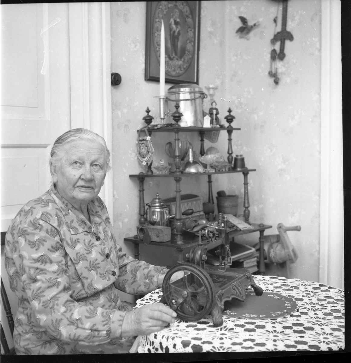 Oidentifierad äldre kvinna sitter vid ett bord med gammal symaskin. Sannolikt i Lommaryd.