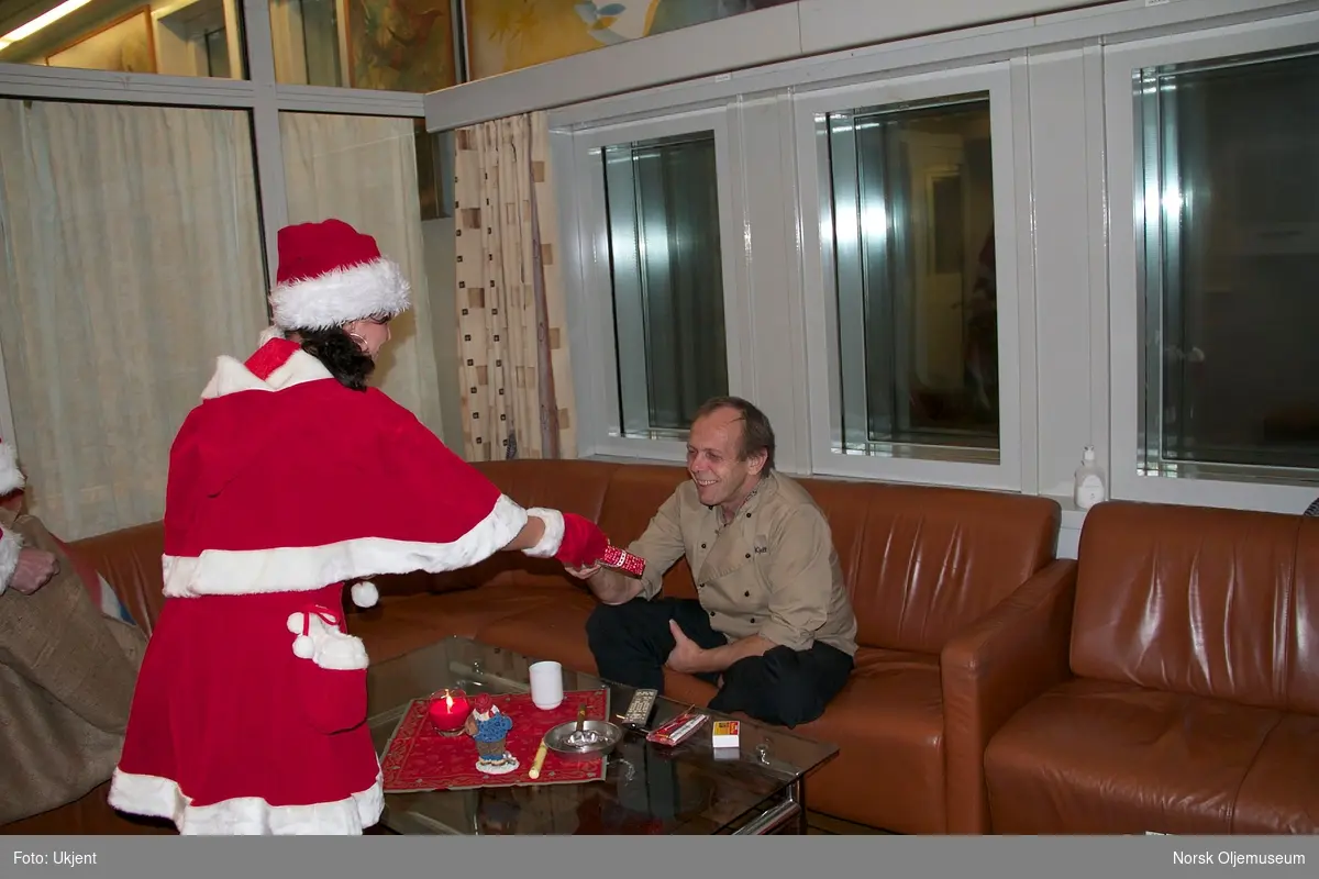 Nissen og assistenten, henholdsvis ...??.... og...?.... deler ut gaver til en person som sitter i røykerommet på Draugen julaften 2010.