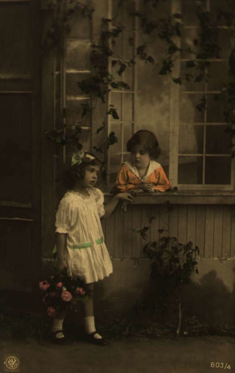 Postkort. Håndkolorert fotografi. To piker står ved et vindu og prater. Stemplet 04.11.1923