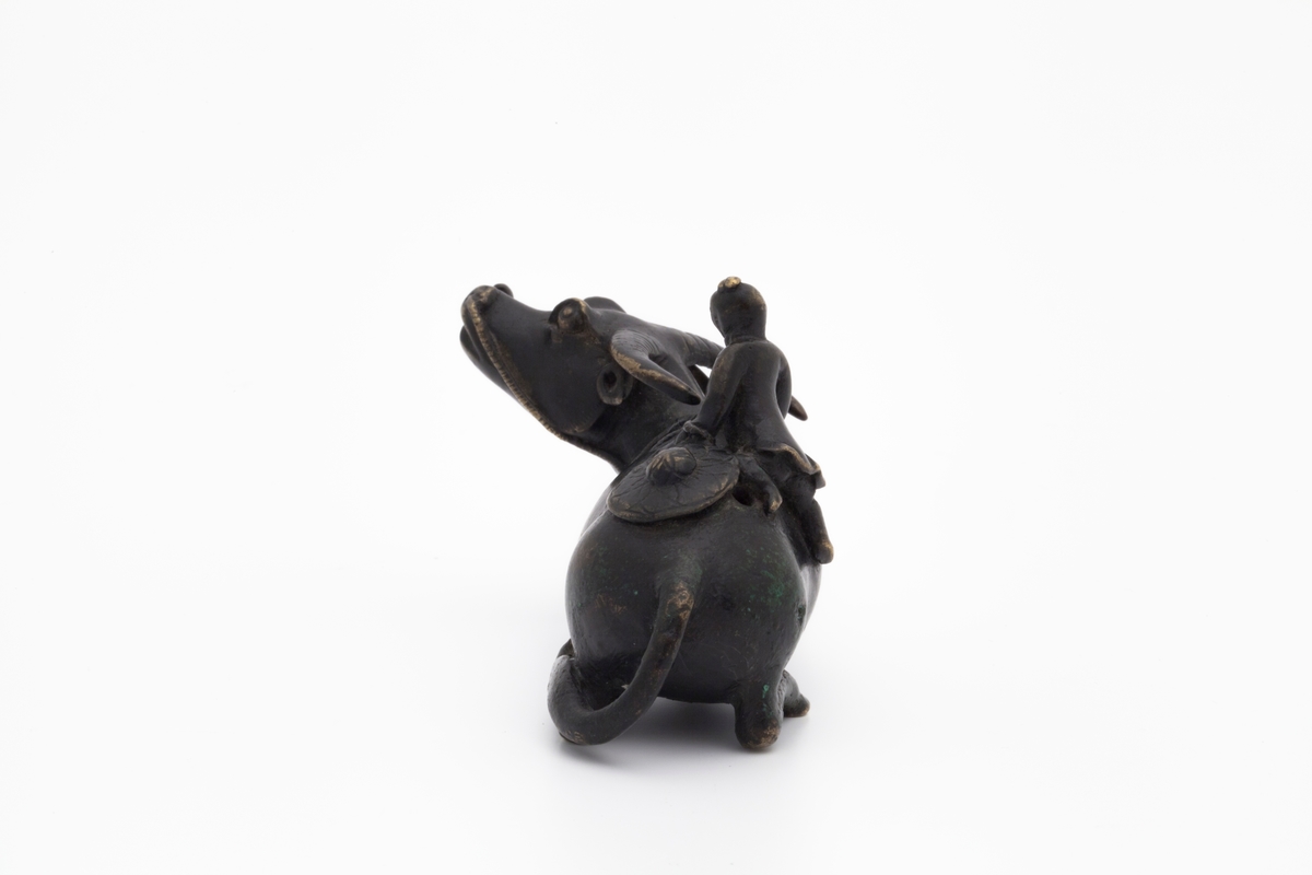 Vanndrypperen forestiller en mannsfigur som bestiger en vannbøffel. Han holder tauet festet til bøffelens mule i den ene hånden mens han løfter seg opp med den andre. Bak på ryggen ligger hatten hans, som er rikt dekorert.