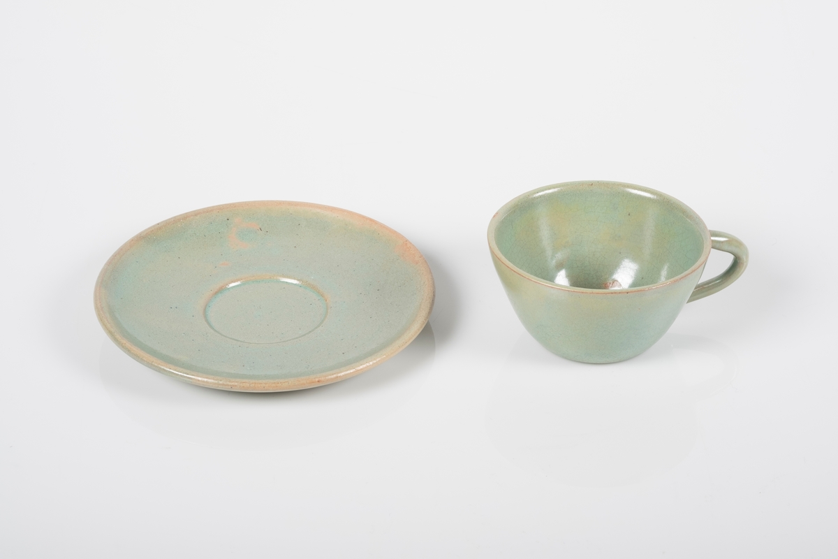 Kopp med skål i keramikk med grønn lasur. Buet hank på koppen. To små knotter (mangler en tredje knott) på undersiden av koppen, usikker funksjon. Skålen er blank på oversiden og matt på undersiden.