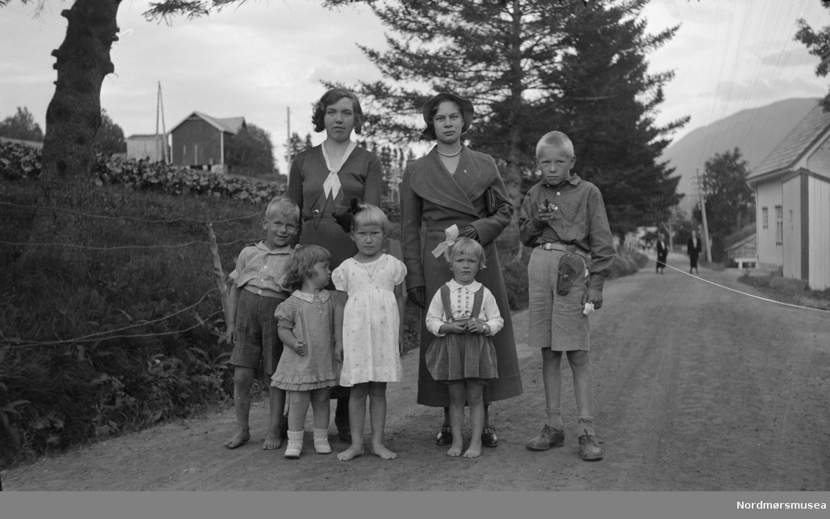 To kvinner ute på tur med fem barn hvorav den ene er "bevæpnet". Trolig fra Sverdrupfamilien, med Georg Sverdrup som sannsynlig fotograf. Usikkert hvor, men kan nok være på Eidsvåg i Nesset kommune. Fra Sverdrupsamlingen ved Nordmøre museums fotosamlinger.