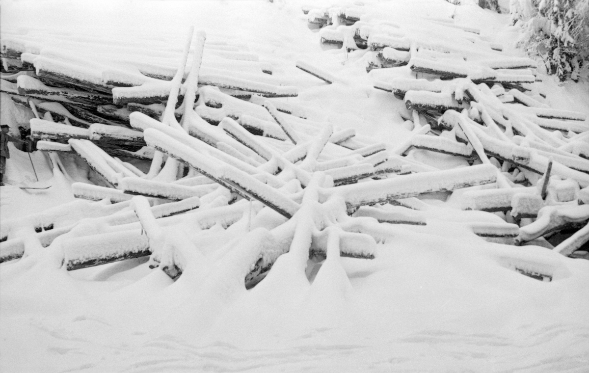 Utrast virke fra Arnestadvelta ved Hovda i Åmot.  Fotografiet er tatt vintertid, antakelig på tvers av et is- og snødekt elveleie mot en skråning, der tømmerstokkene er trillet ned mot vassdraget.  Stokkene ligger noe hulter til bulter, men i hovedsak parallelt med strømretningen.  På denne måten ble det naturligvis en arbeidskrevende oppgave å få slått tømmeret ut i elve når fløtingssesongen startet.   

Hovda med sidevassdrag har et nedslagsfelt på drøyt 190 kvadratkilometer.  Det var mulig å fløte helt fra innsjøen Storhovden, men i den øverste delen av vassdraget var det langtfra sikkert at tømmeret nådde Glomma i løpet av første fløtingssesong.  Først fra sammenløpet med elva Hemla ble fløtinga ansett for å være «sikker».  På denne strekningen rant elva østover, og det var tett mellom velteplassene.  Arnestadvelta lå cirka 6 kilometer i luftlinje øst for det stedet der de to elvene møttes.  Navnet skyldes antakelig at det i hovedsak var tømmer fra skogen til garden Arnestad i Åmot som ble levert på dette stedet.   Våren 1951, etter den driftssesongen i skogene som var i gang da dette fotografiet ble tatt, var det innmeldt 31 458 tømmerstokker til fløting i Hovda.